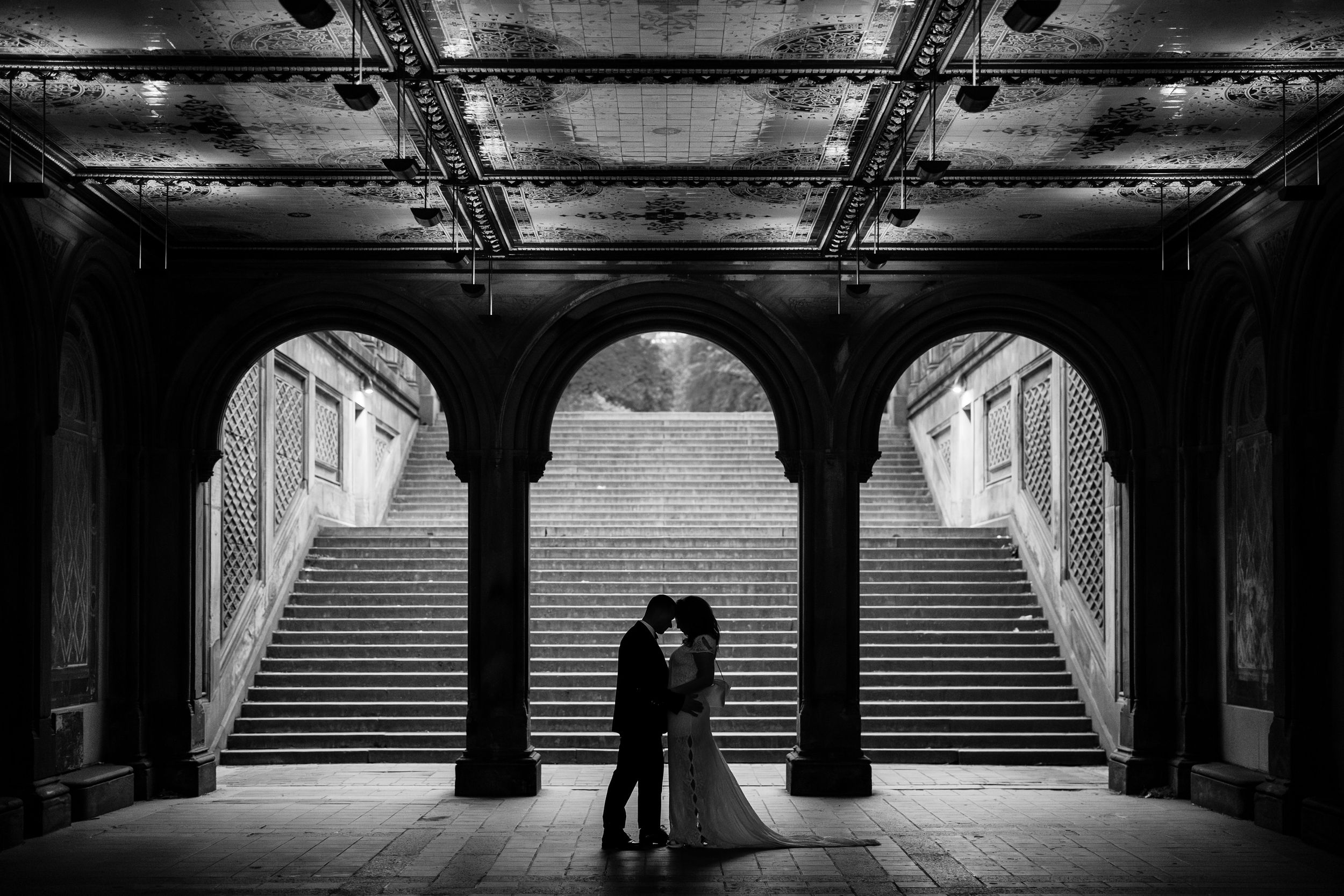 Black and white architectural photograph of a symmetrical underground walkway with dramatic lighting and arched columns.