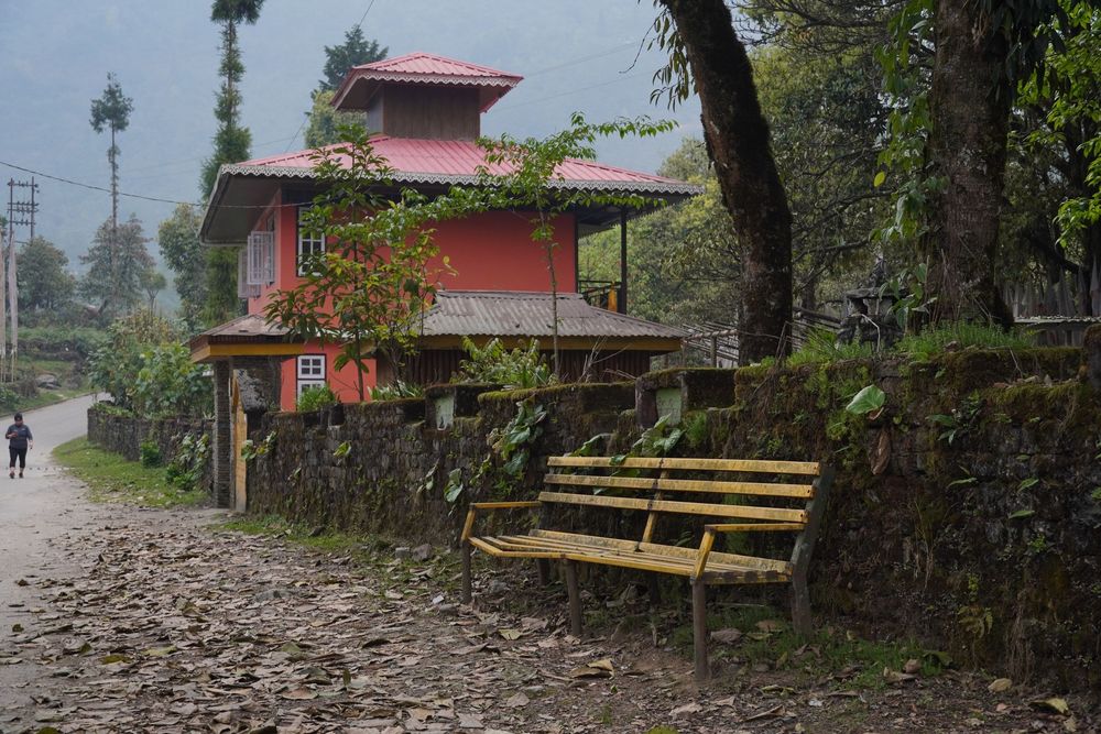 A traditional red-roofed mountain house and an empty yellow bench, capturing the quiet solitude of a Himalayan village.