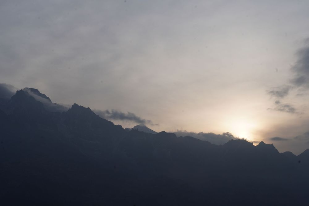 A sprawling mountain peak partially hidden by dense clouds and misty light during a high-altitude Himalayan trek.