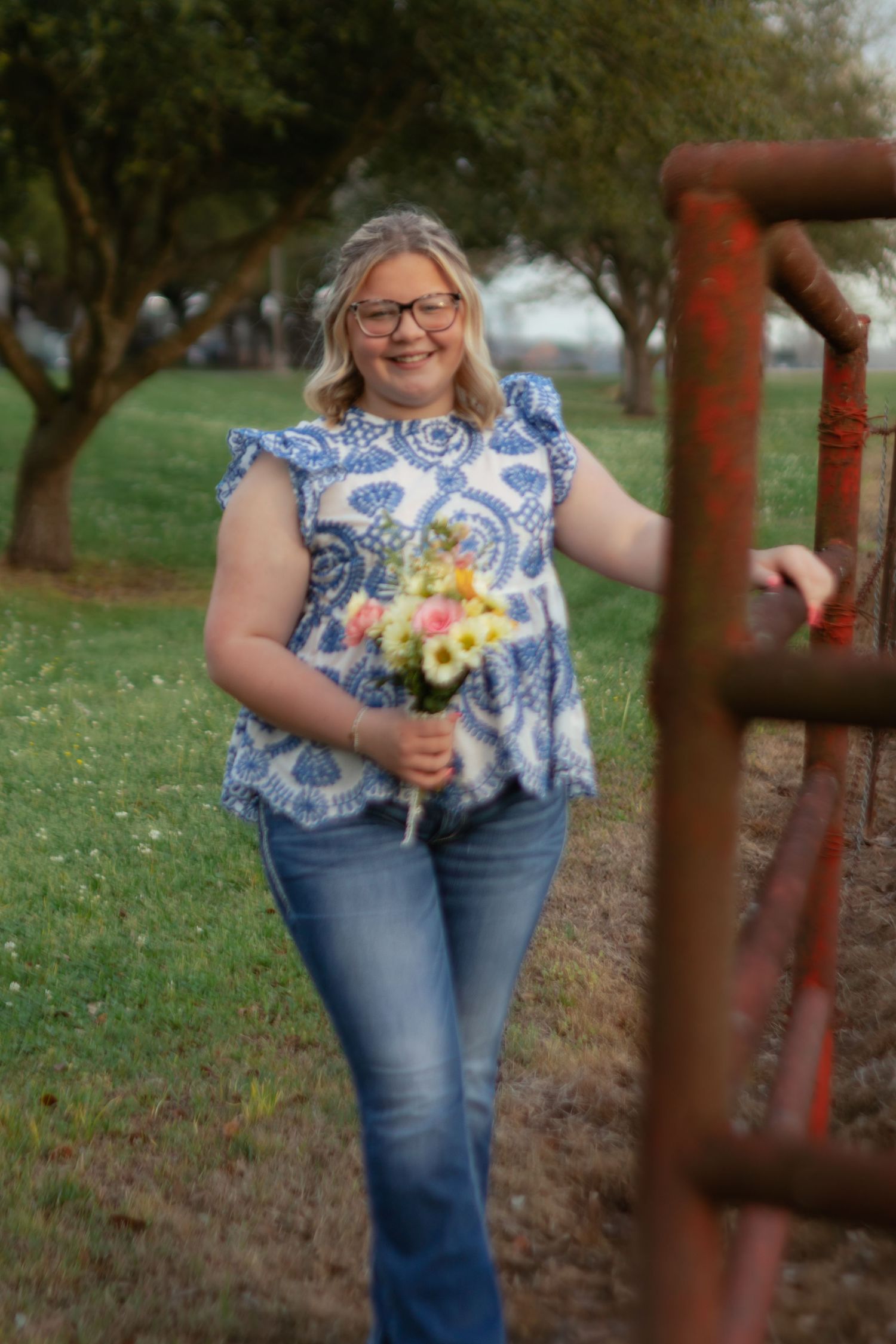 Someone wearing a blue and white patterned top and jeans holds a colorful bouquet in an outdoor garden setting.