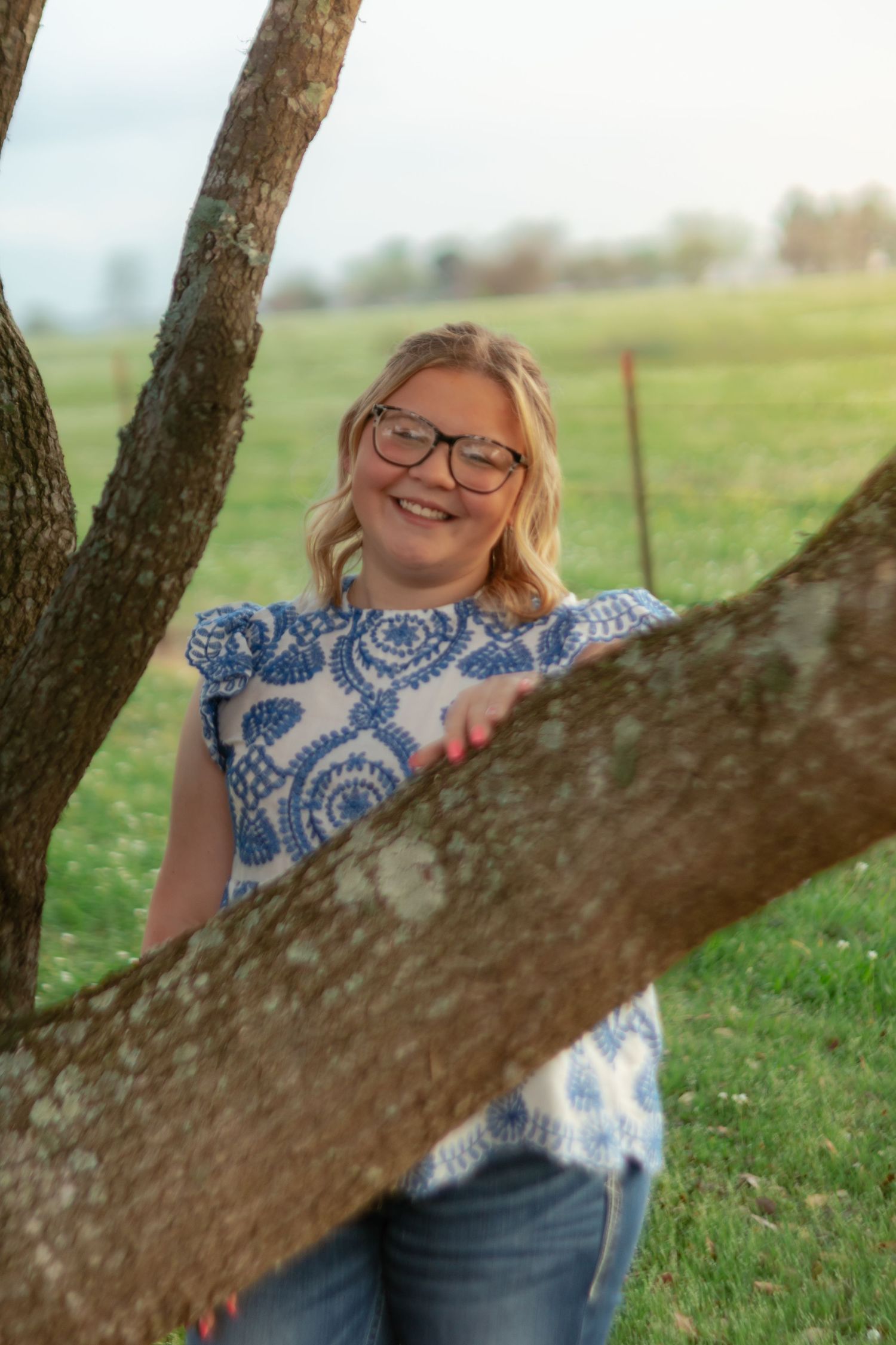 A person wearing a blue and white patterned top relaxes against a tree trunk in a sunny meadow.