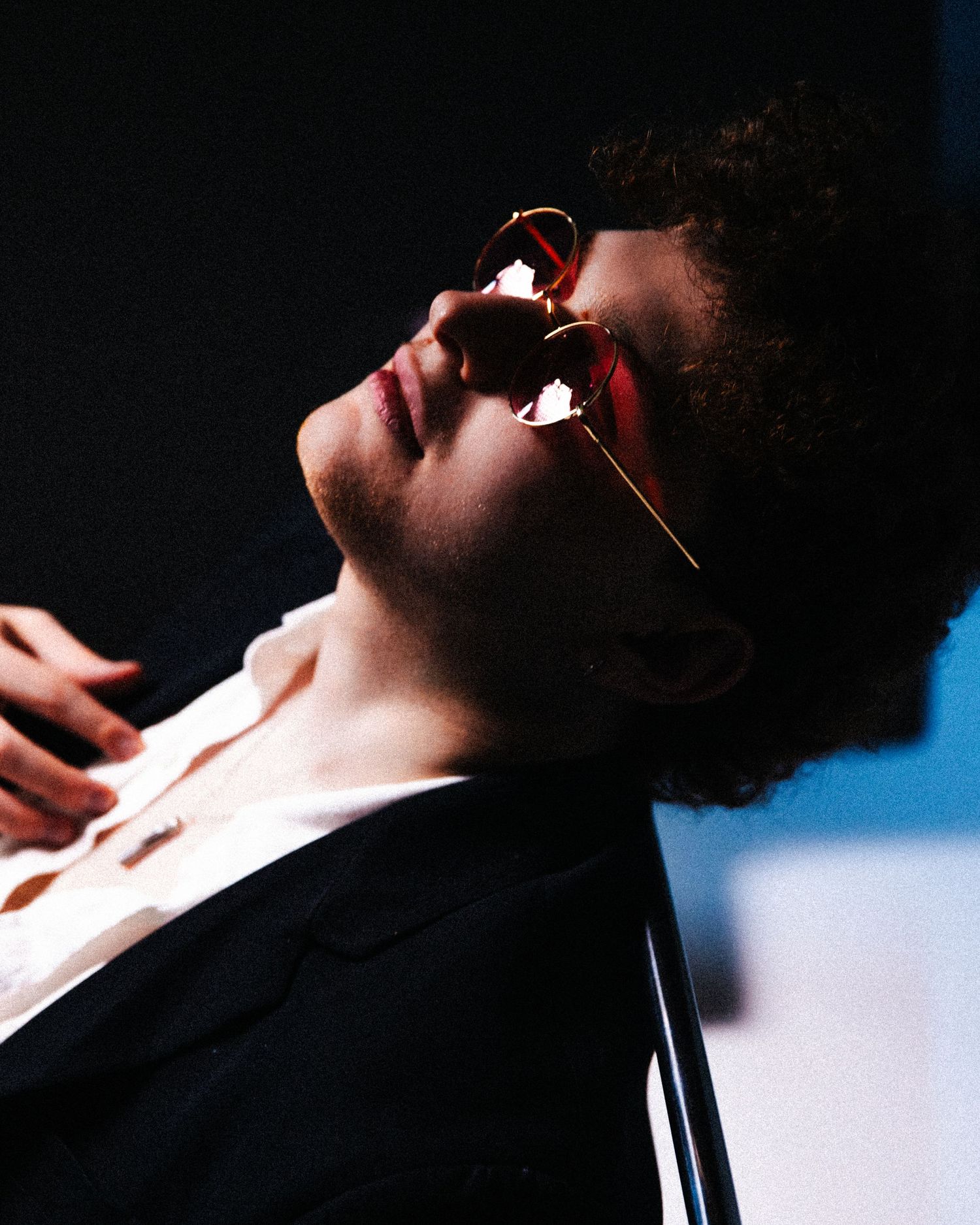 A person in profile view singing or performing against a dark background with dramatic lighting effects.