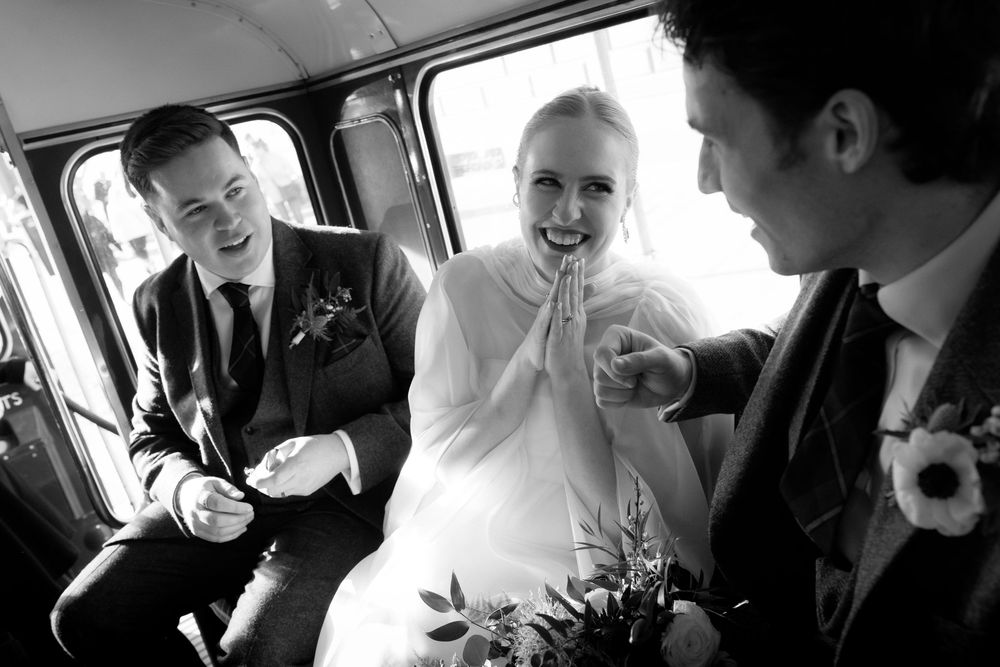 A candid black and white photograph of wedding party members sharing a joyful moment together in a vehicle.