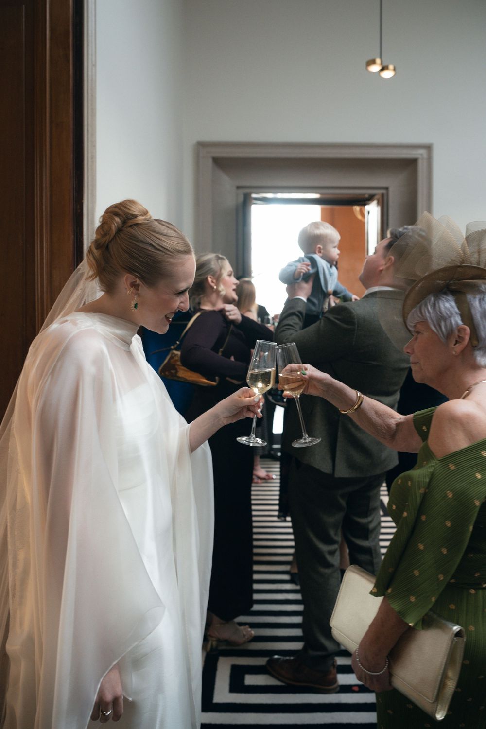 People in formal attire mingle and socialize at an elegant reception or gallery event.