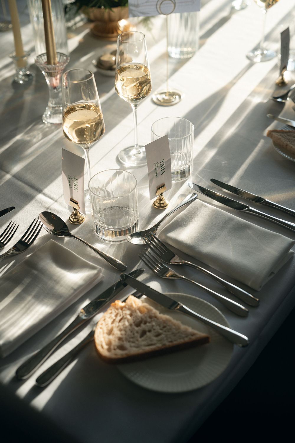 Elegant table setting with wine glasses and bread on a black tablecloth casting dramatic shadows in natural light.