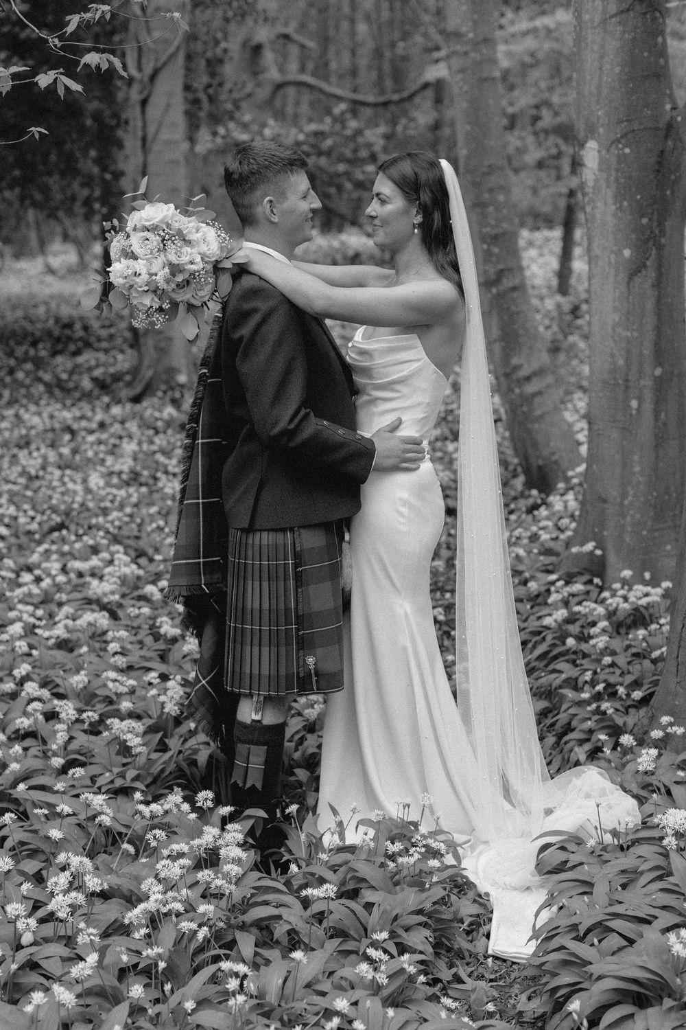 A romantic wedding moment captured in black and white as newlyweds embrace in a forest setting.