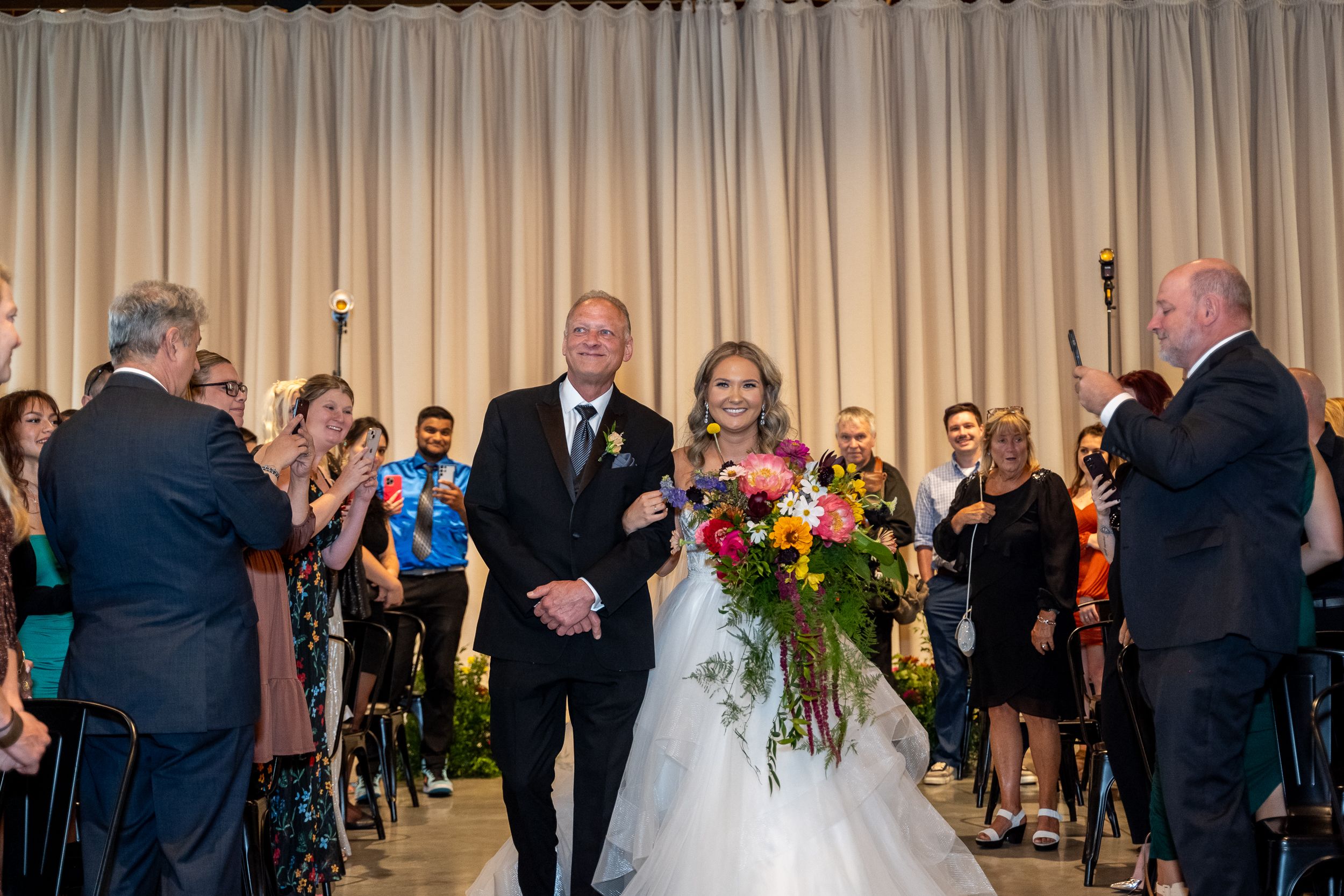 Wedding ceremony attendees gather in an elegant venue with beige curtains and warm lighting for a special celebration.
