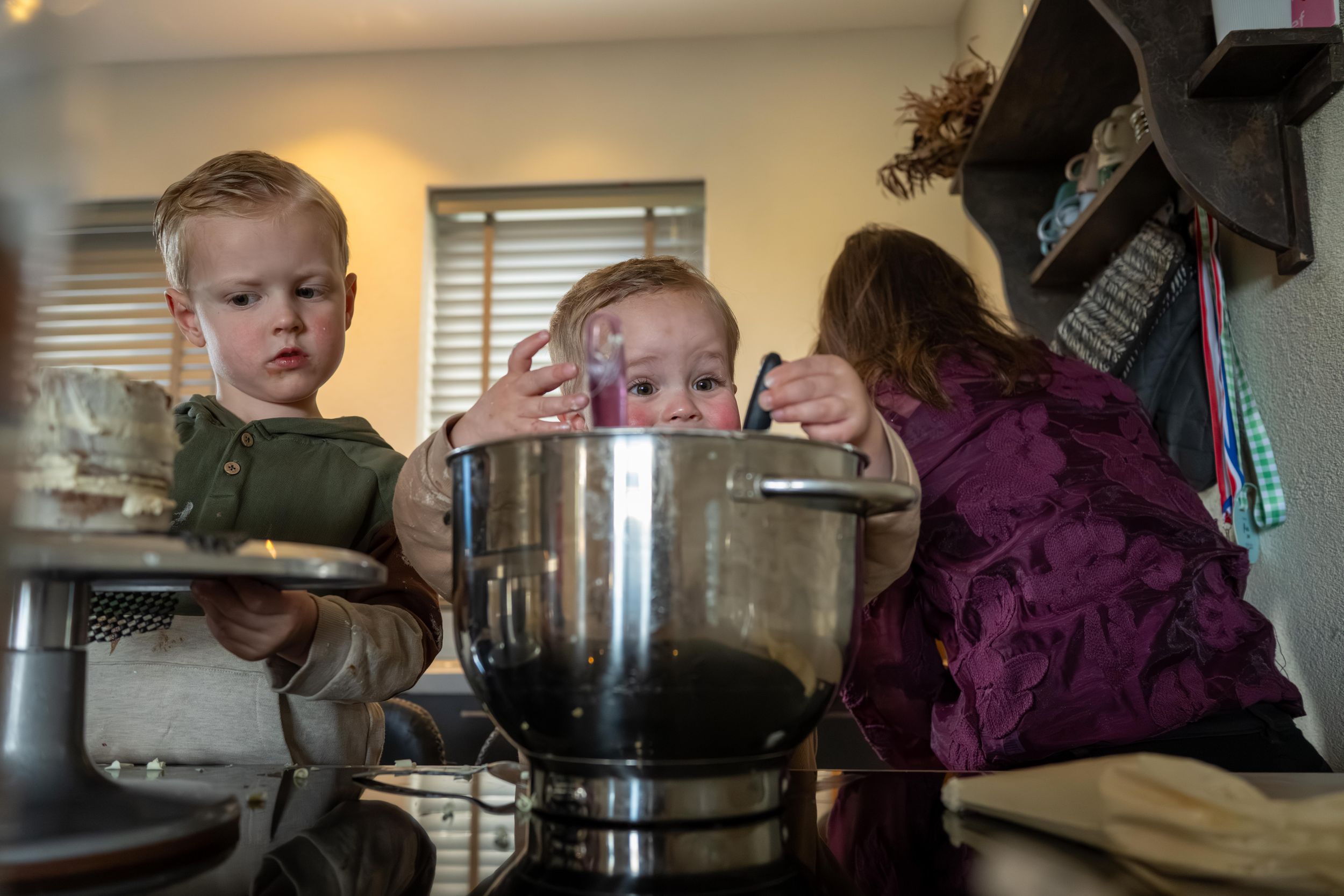 Children gather around a large metal pot in a kitchen while cooking or baking together.