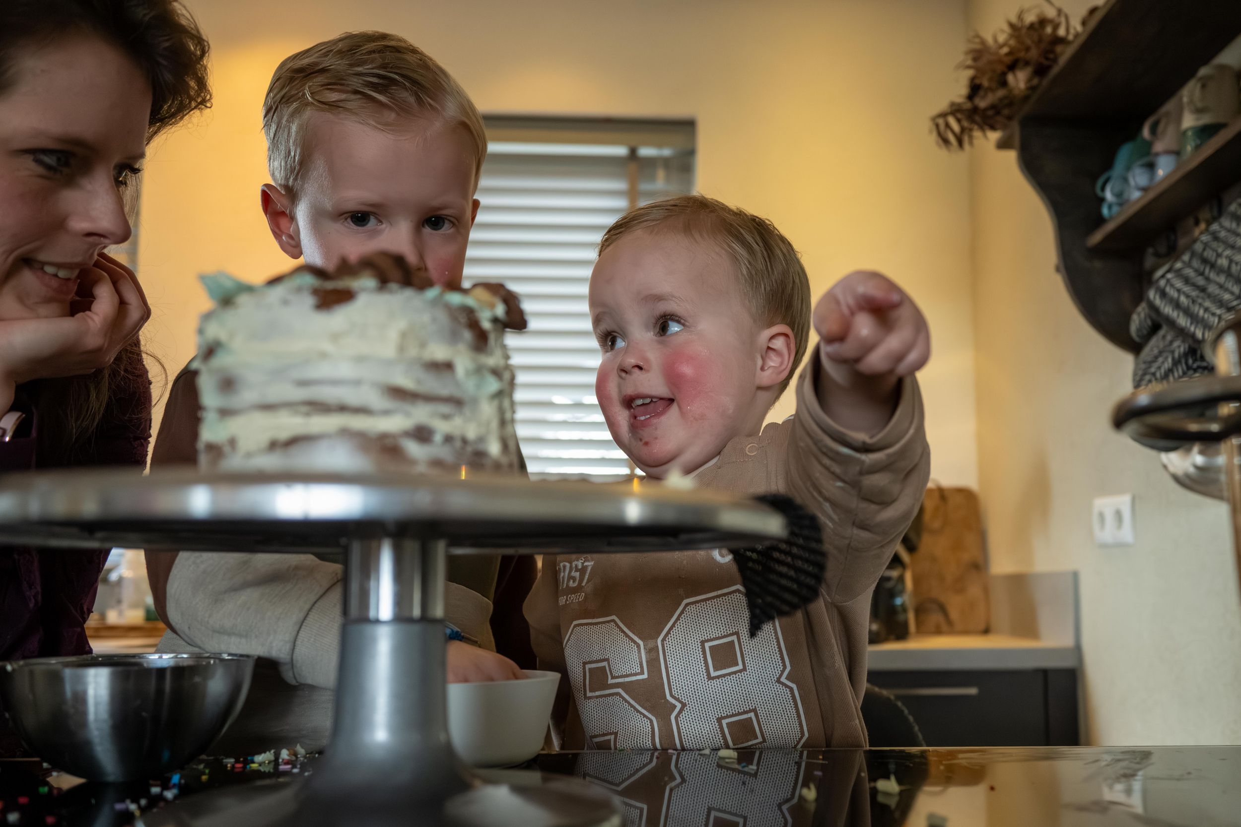 Family gathered around a wooden dining table with a birthday cake and candles in warm lighting.