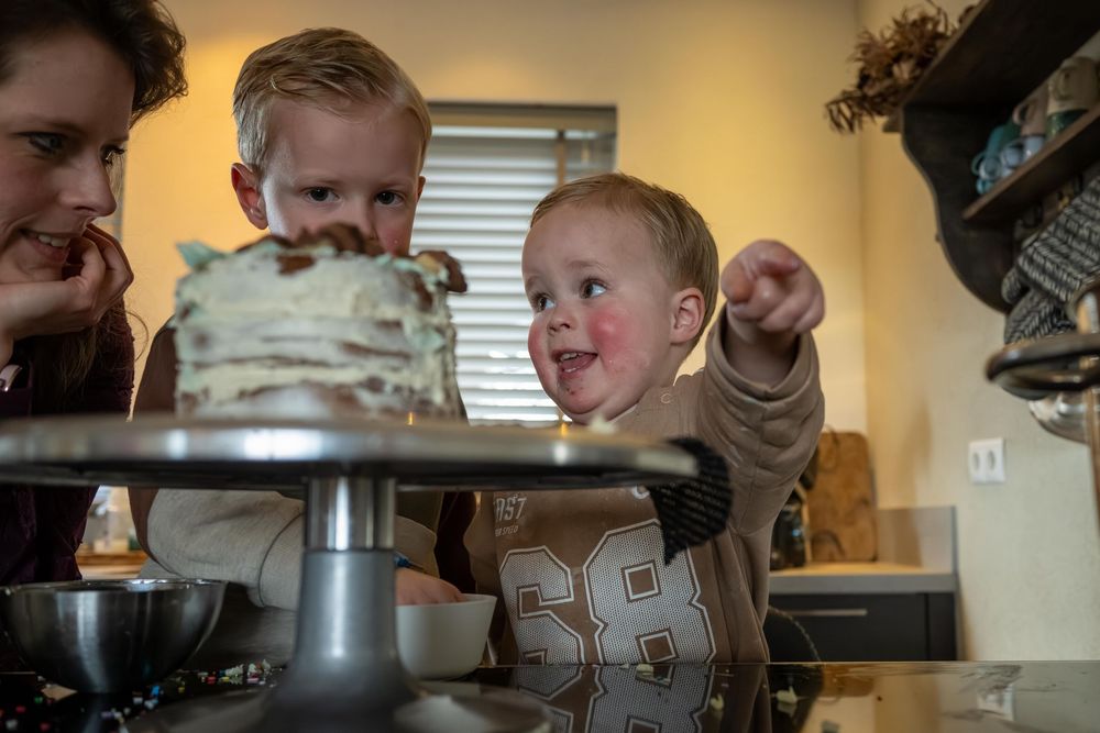 Family gathered around a wooden dining table with a birthday cake and candles in warm lighting.