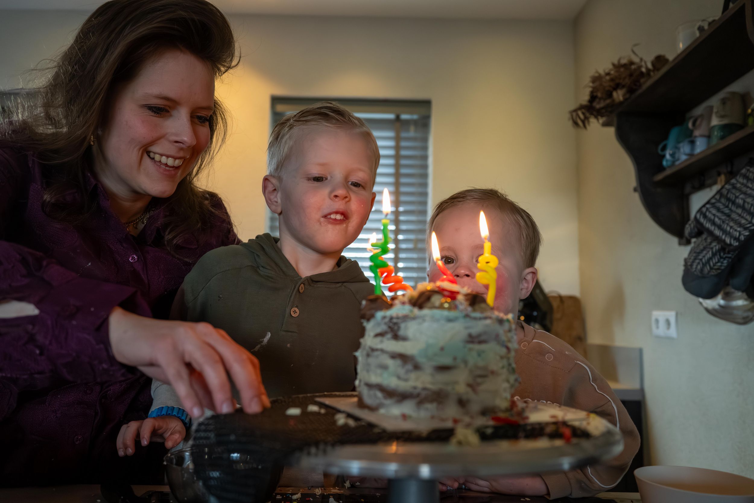 A birthday celebration around a cake with lit candles glowing warmly in an indoor setting.