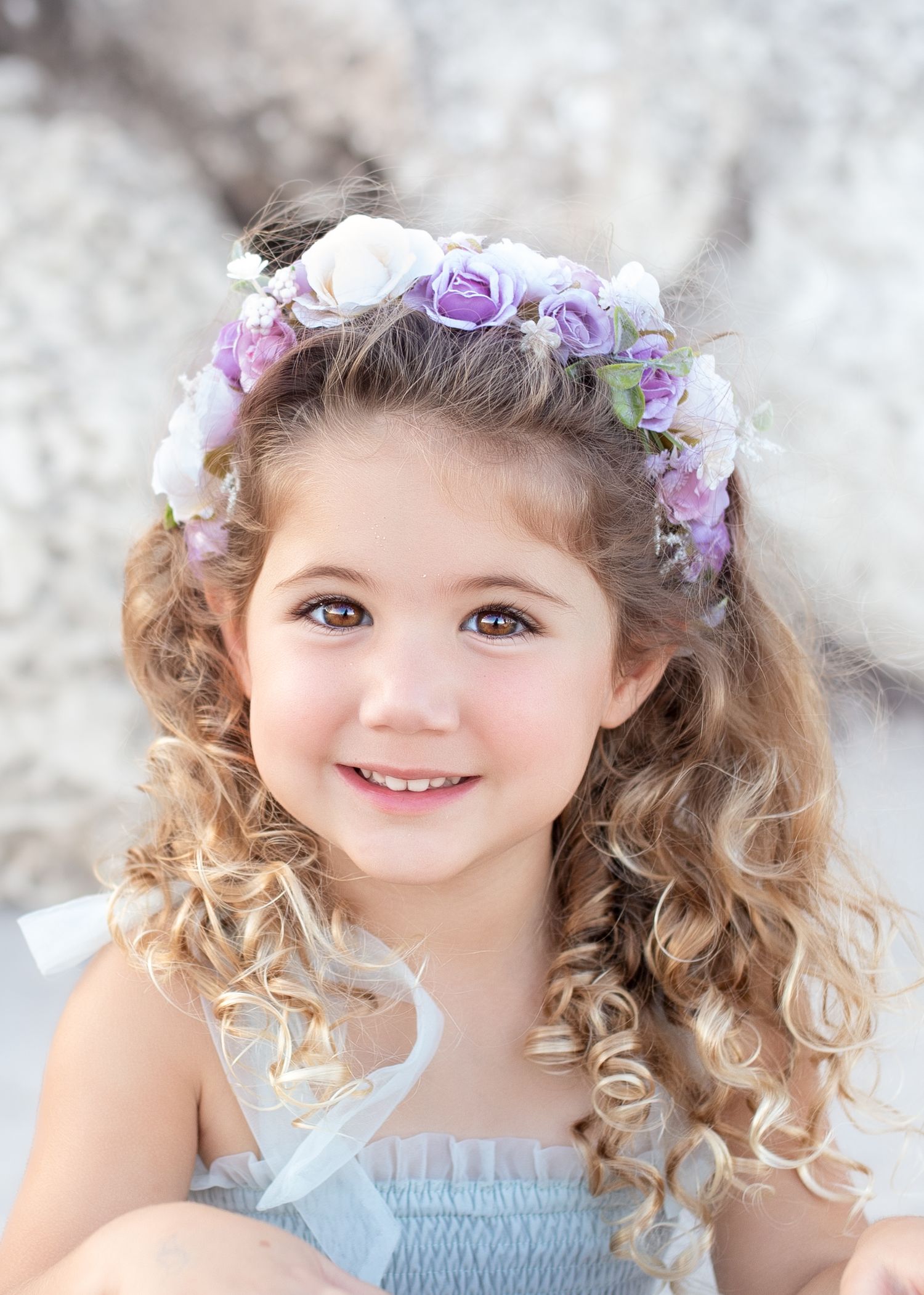 A child wearing a floral crown and light blue dress smiles brightly in a series of three portrait photos.