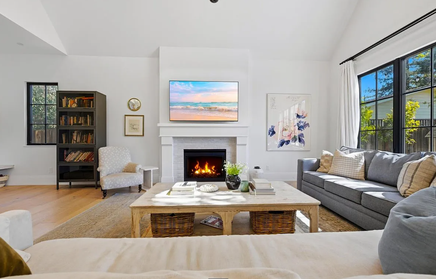 Modern open concept living room with white walls, hardwood floors, fireplace and large windows overlooking water views.