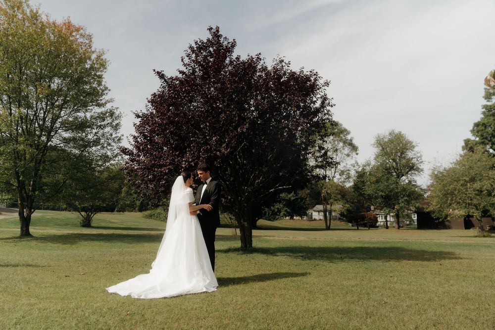 A bride and groom share a romantic moment on a lush green lawn surrounded by trees on their wedding day.