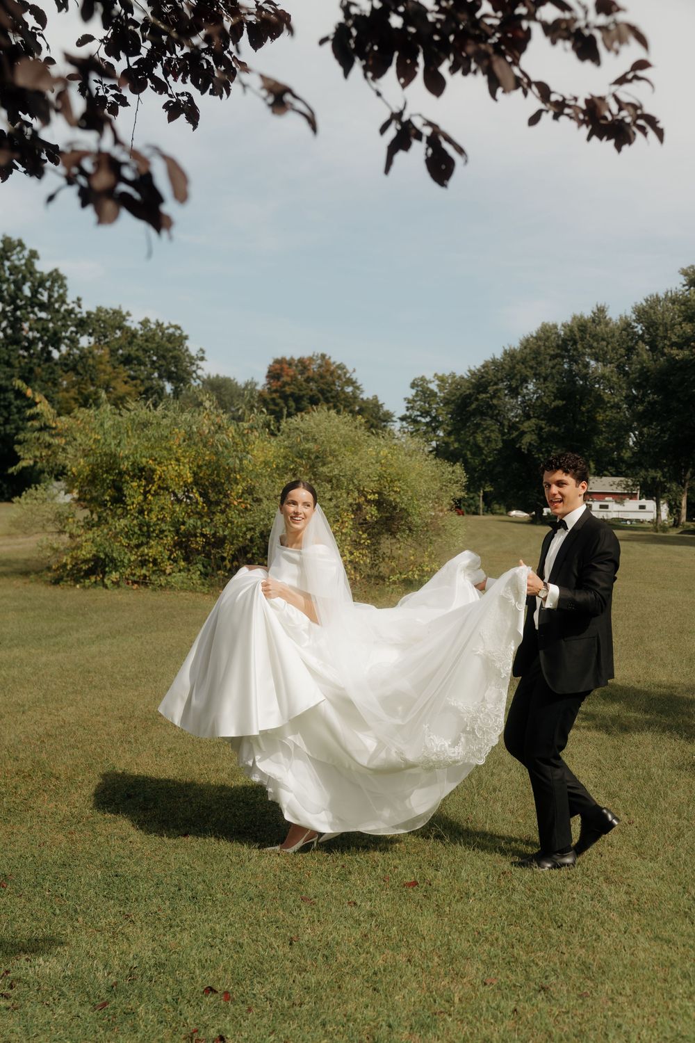 Bride and groom dancing outdoors on green lawn, bride in flowing white ball gown wedding dress.
