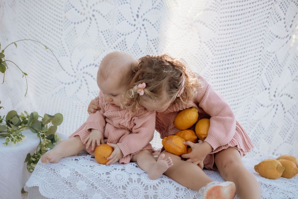 Hands reaching for fresh kumquats on a white lace tablecloth with delicate floral patterns.