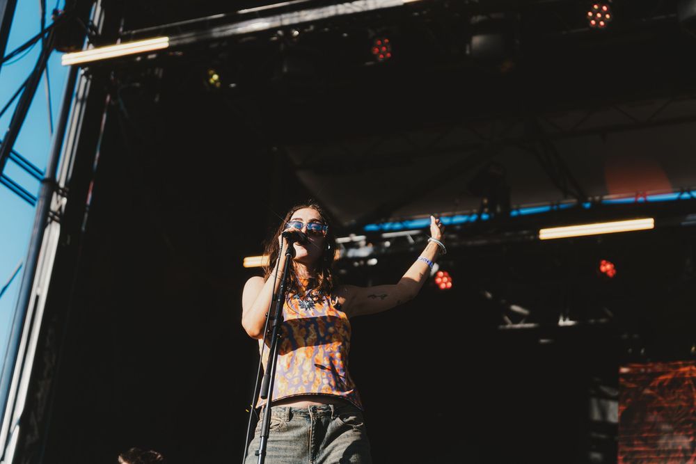 A performer sings passionately on stage during an outdoor concert with stage lighting visible in the background.