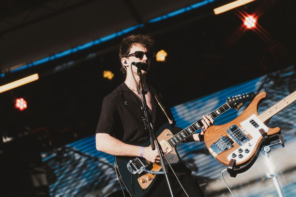 Guitarist performing on stage with blue lighting and holding an electric guitar during a live music performance.