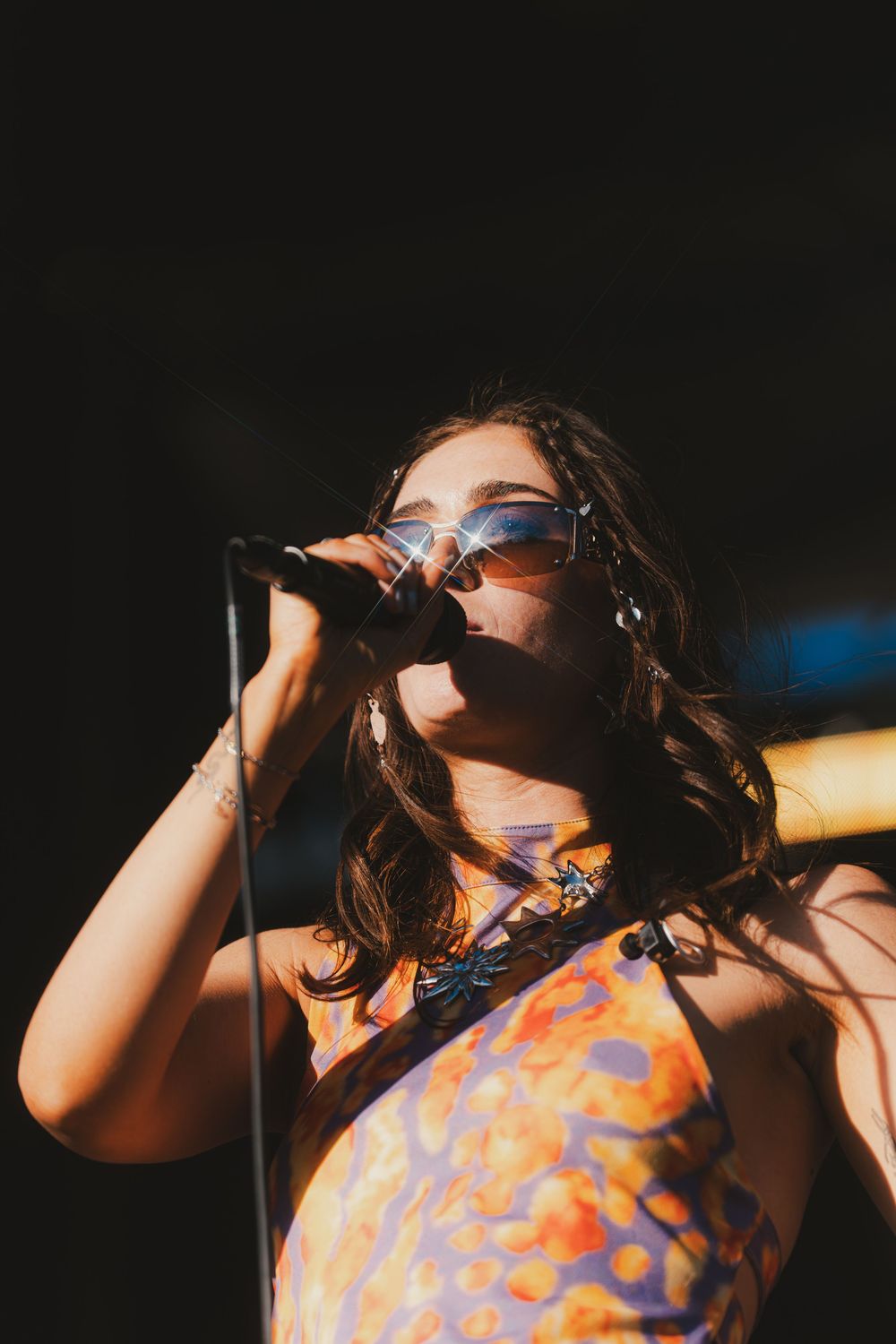 Singer in an orange patterned dress performs on stage under dramatic lighting.