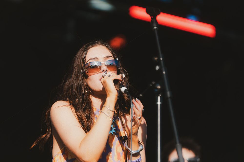 A performer sings passionately on stage holding a microphone under dramatic red lighting during a live concert performance.