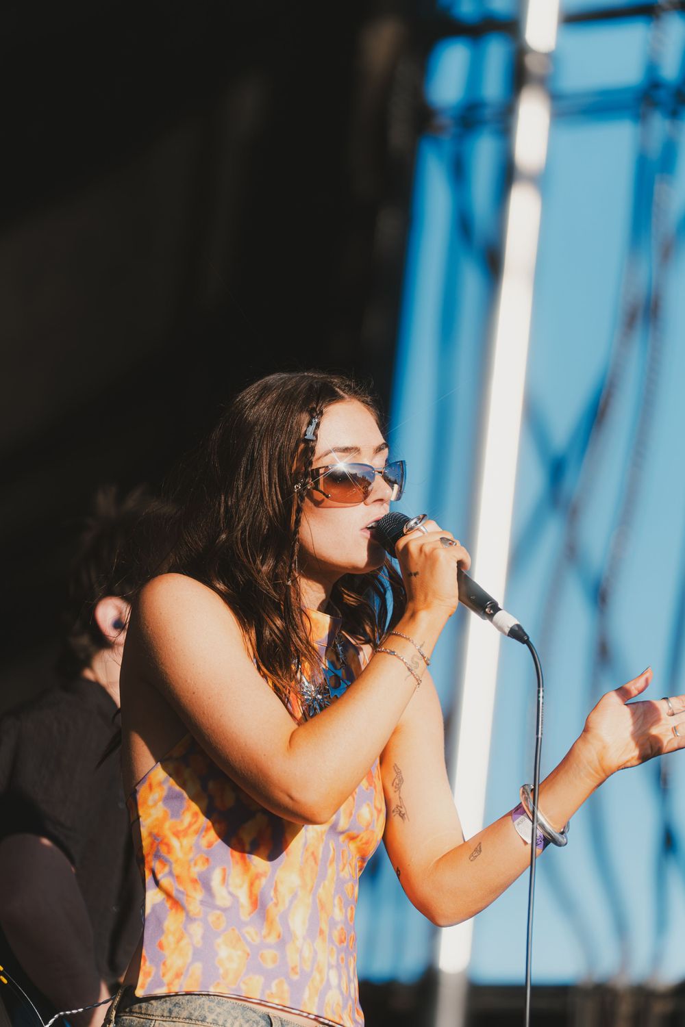 A singer performs passionately on stage wearing an orange patterned dress against a blue-lit backdrop.
