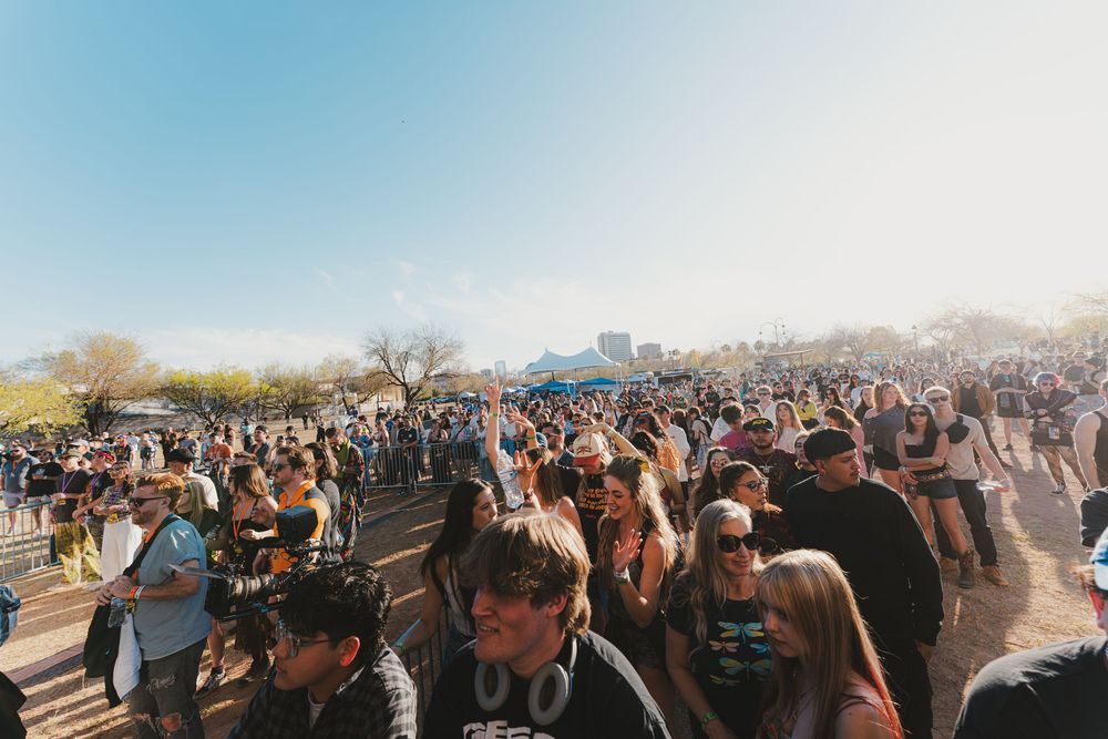 Large crowd of festival attendees gathered outdoors under blue sky during a sunny daytime event.