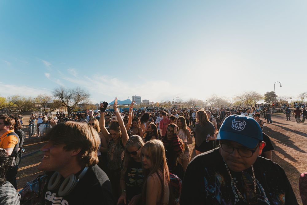 Large crowd of festival attendees gathered outdoors on a sunny day with city skyline visible in the background.