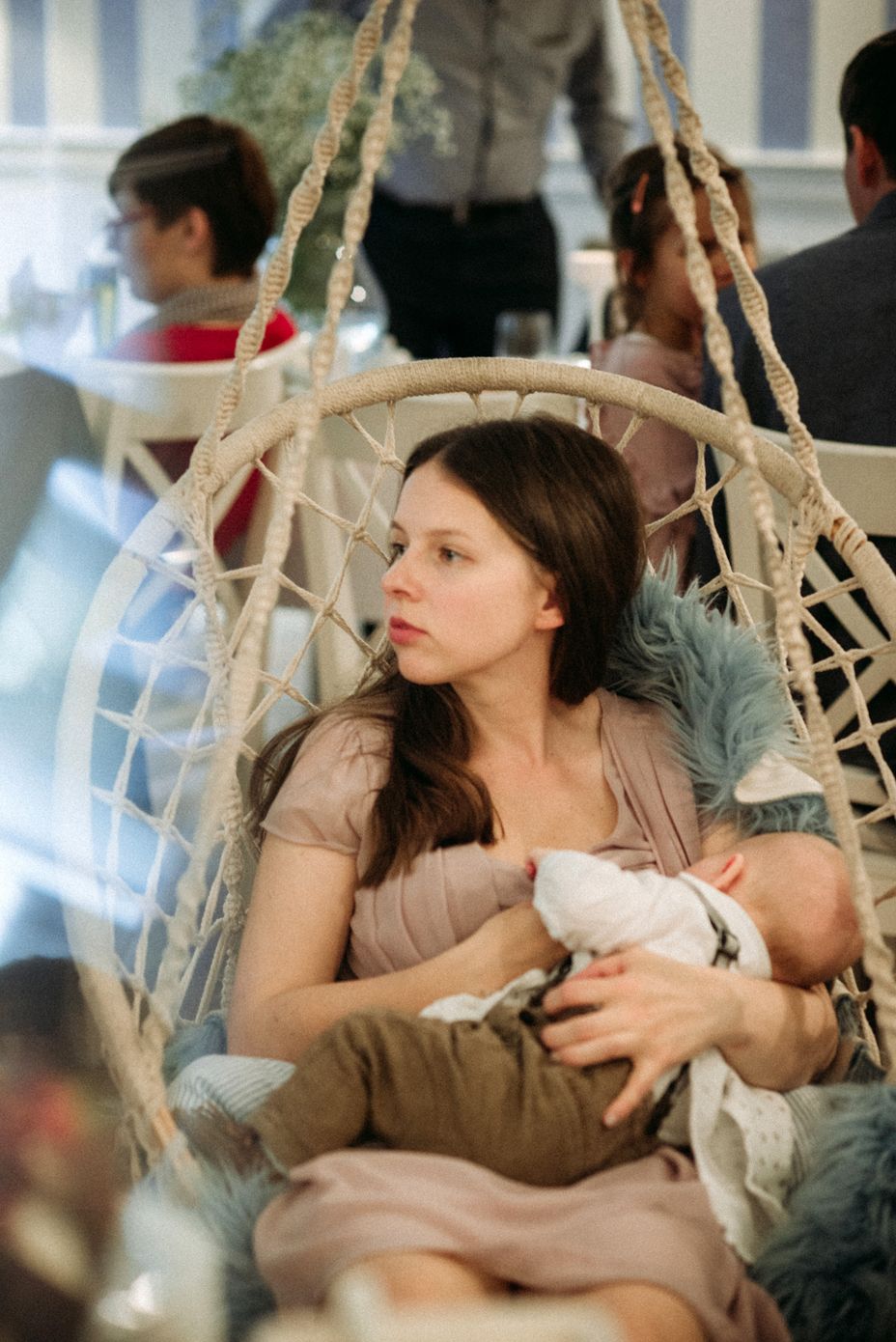 A person relaxes in a hanging macrame chair while holding a small white cat.