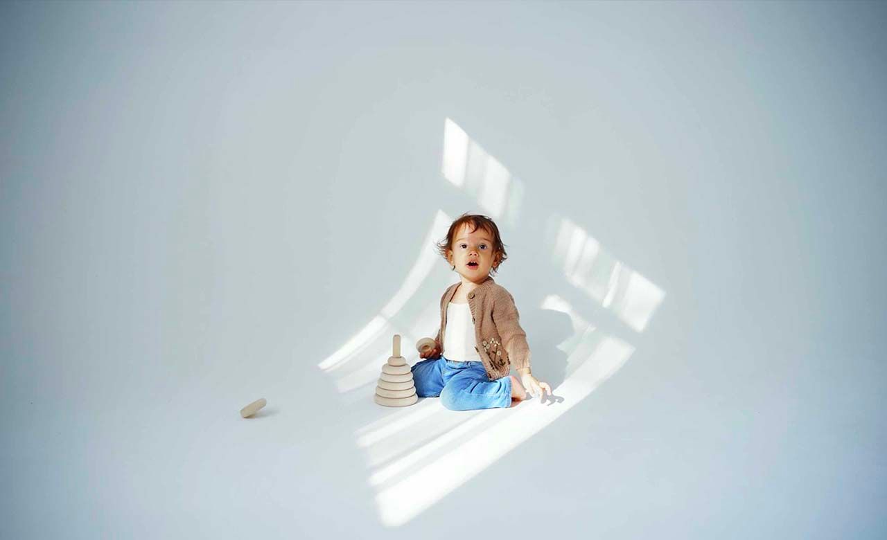 Child sitting in geometric sunlight pattern against light gray wall.