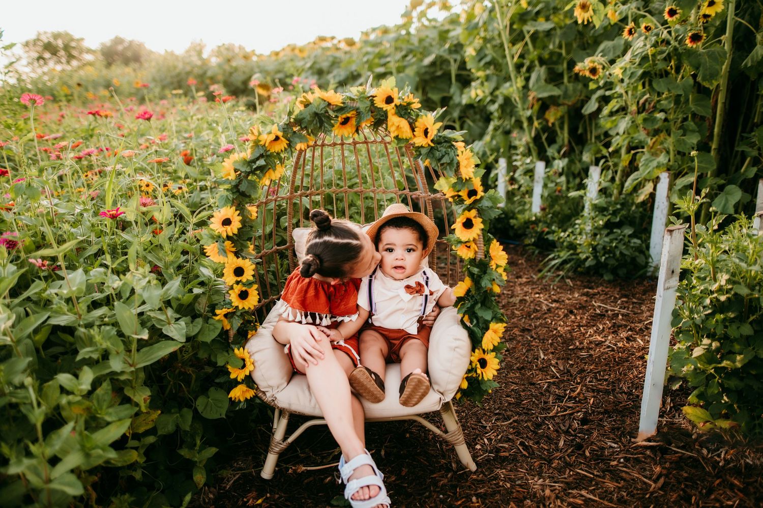Decorative sunflowers adorn a rustic birdcage in an outdoor garden setting.