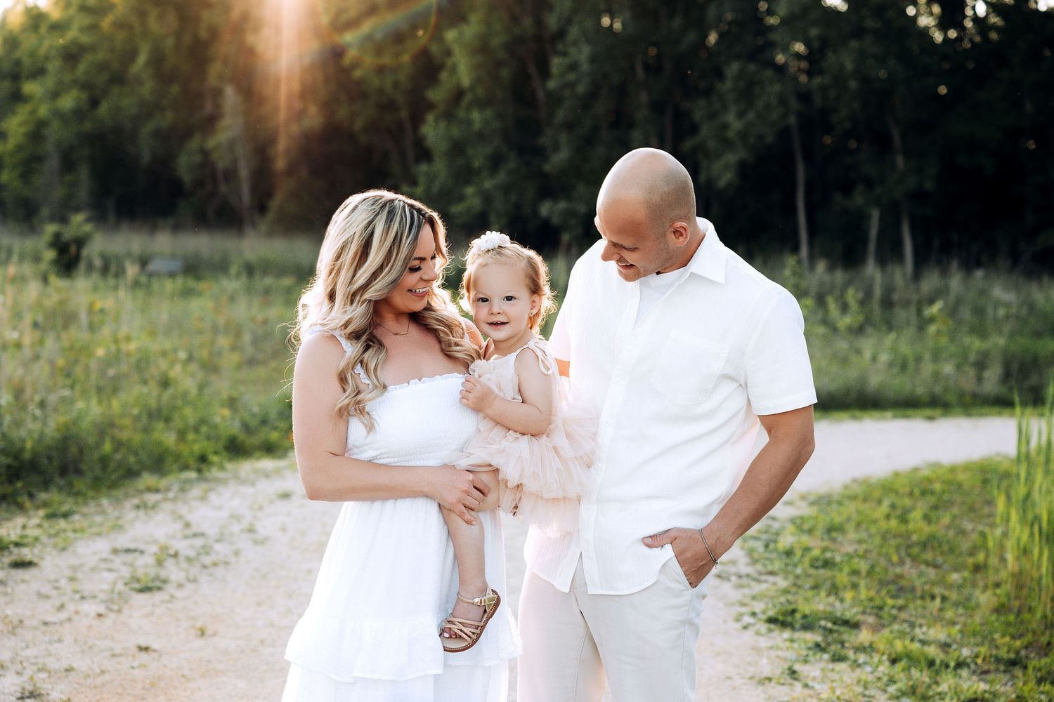 mom and dad looking at their toddler baby girl smiling , sunset session