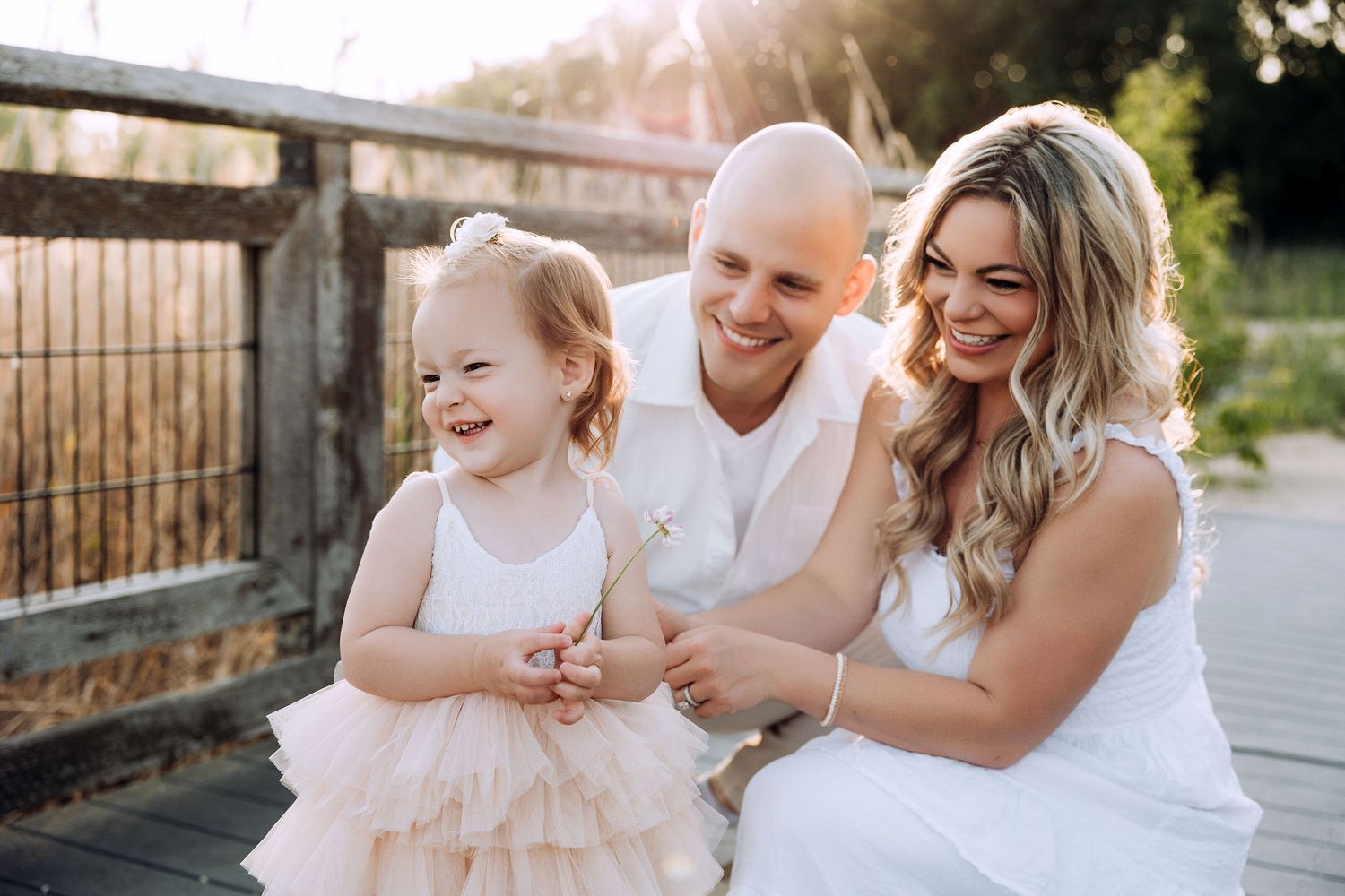 toddler baby girl giggling with a warm sunset sun filling the image and parents watching their baby girl