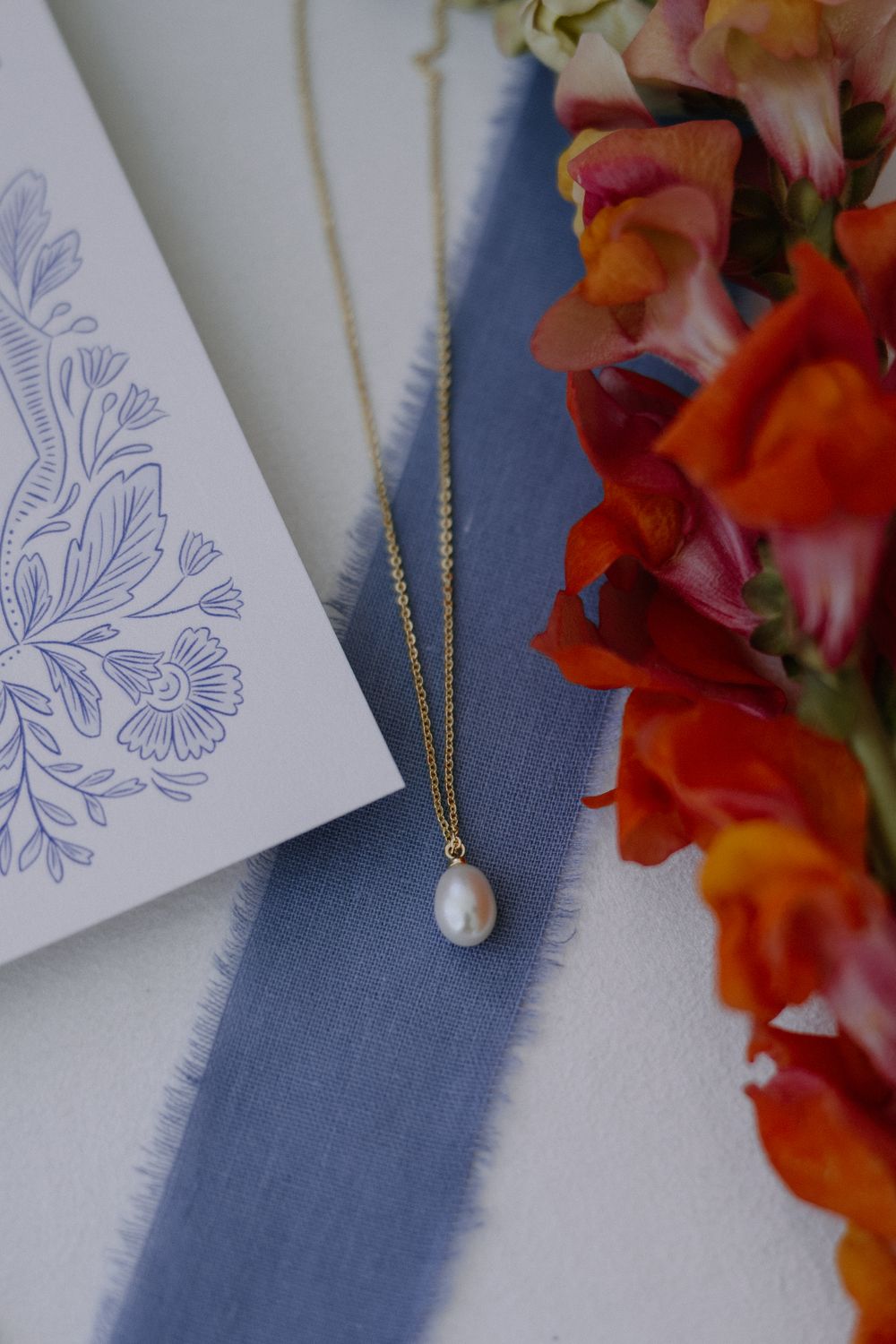 Wedding stationery with floral designs and pearl necklace on blue fabric.