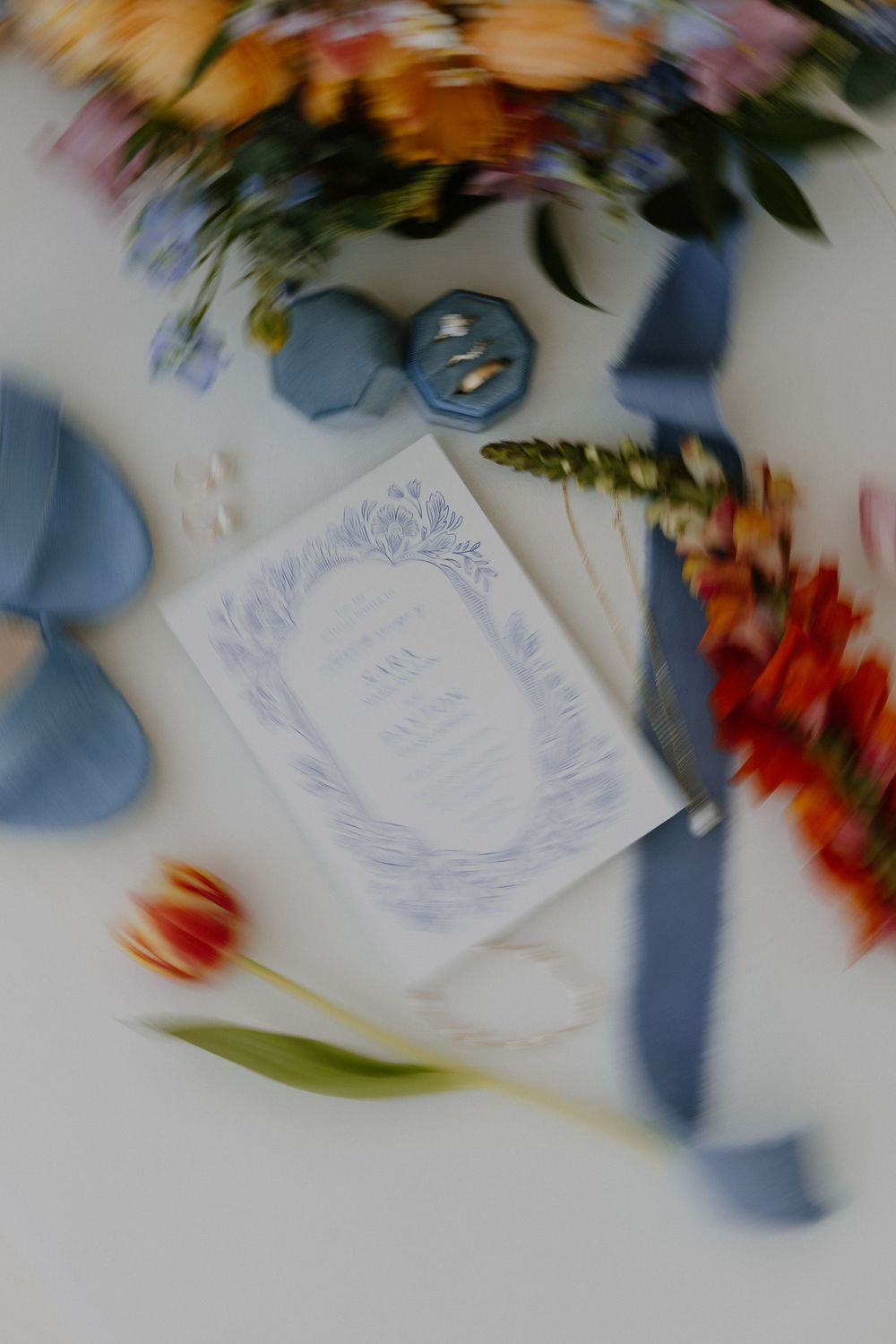Artistic blurred shot of wedding stationery and floral details on white surface.