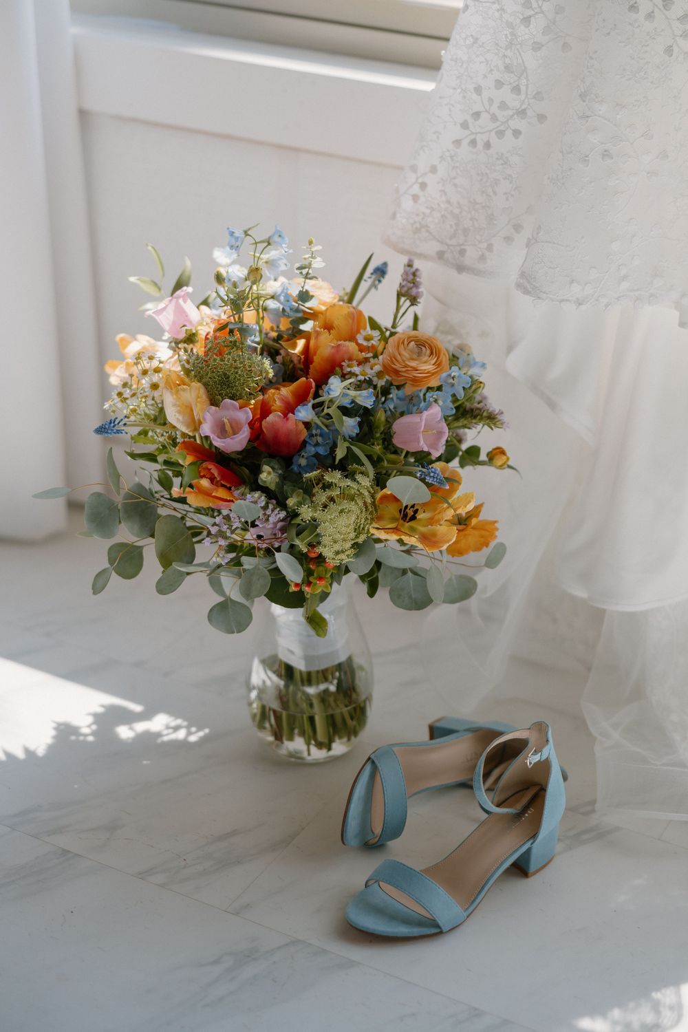 Light blue wedding shoes displayed with colorful floral bouquets featuring orange roses and greenery.