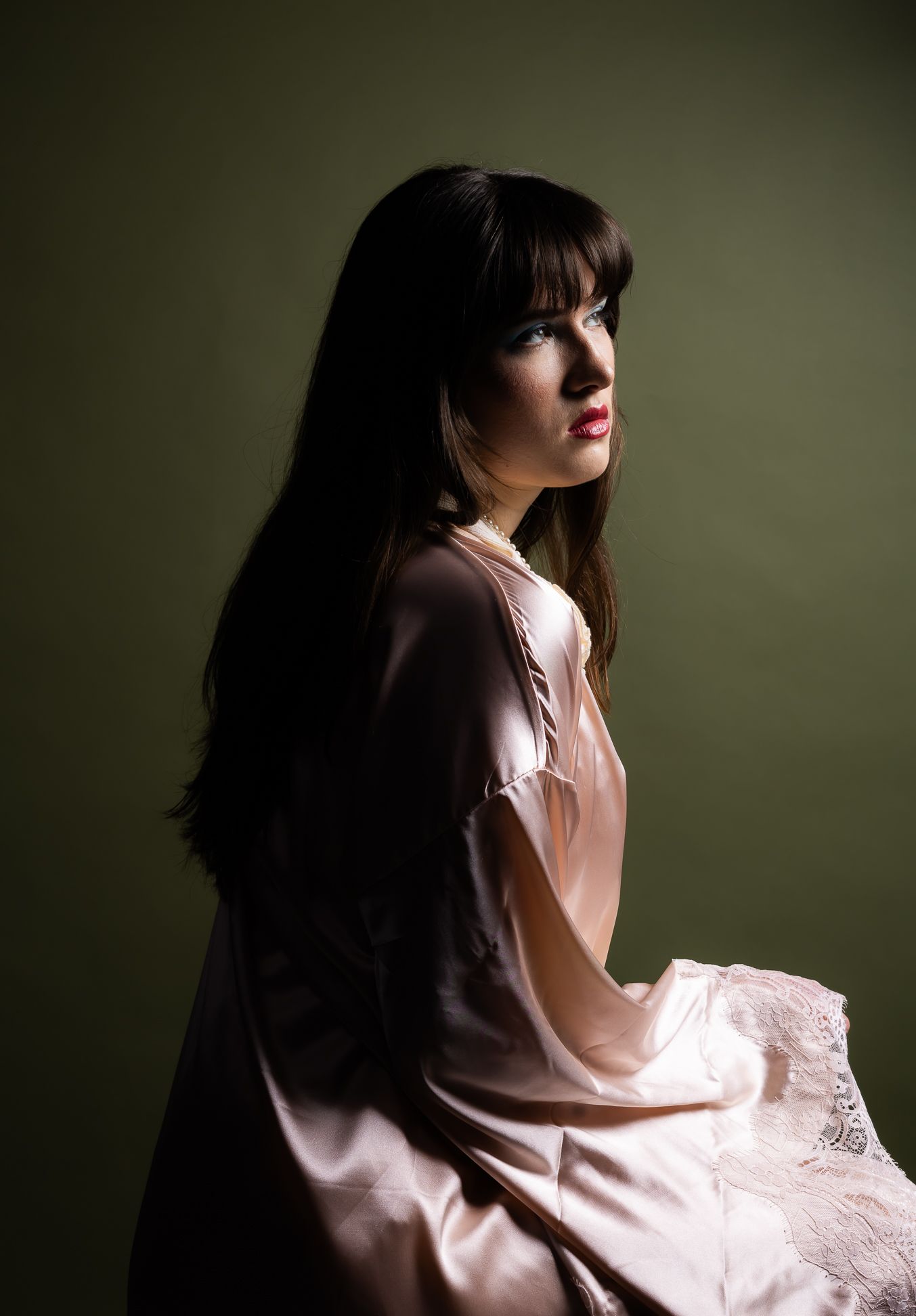 Girl in a pink robe in front of an olive backdrop, looking right