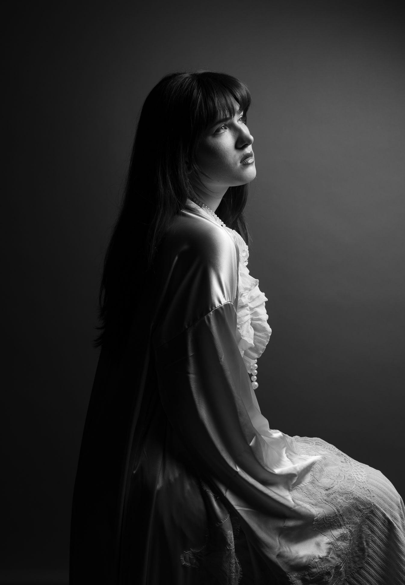 Girl in a pink robe in front of an olive backdrop, looking right and up, black and white photo