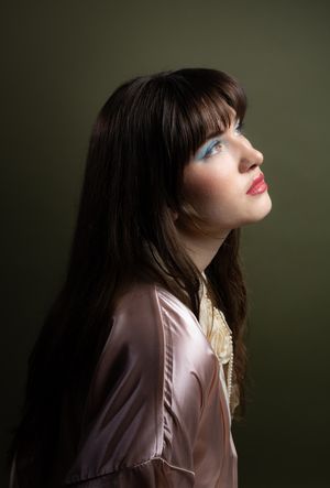 Girl in a pink robe in front of an olive backdrop, looking right and up, side profile