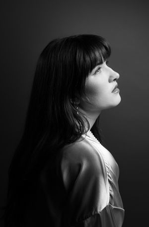 Girl in a pink robe in front of an olive backdrop, looking right and up, side profile black and white image