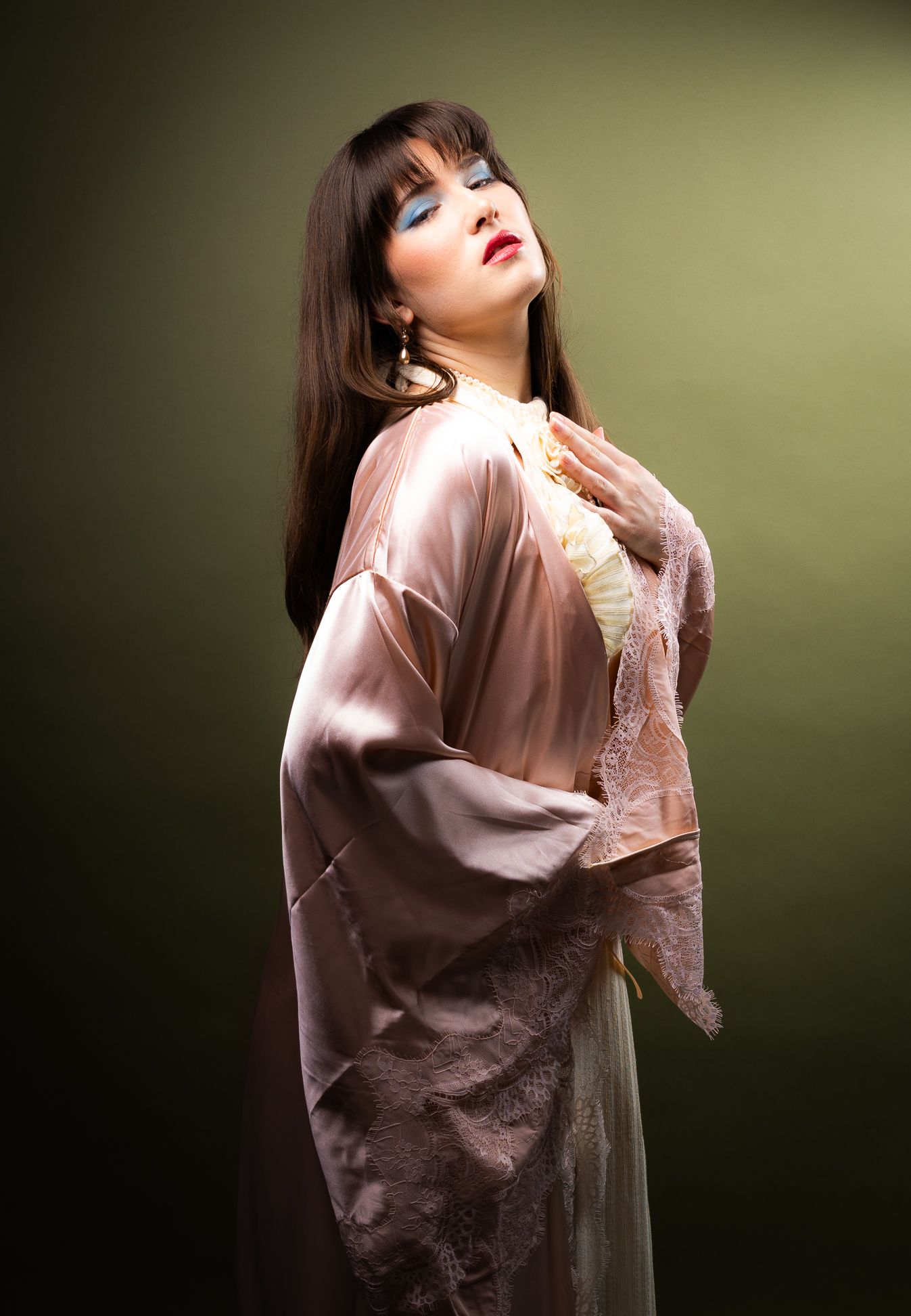 Girl in a pink robe in front of an olive backdrop, looking at the camera, standing
