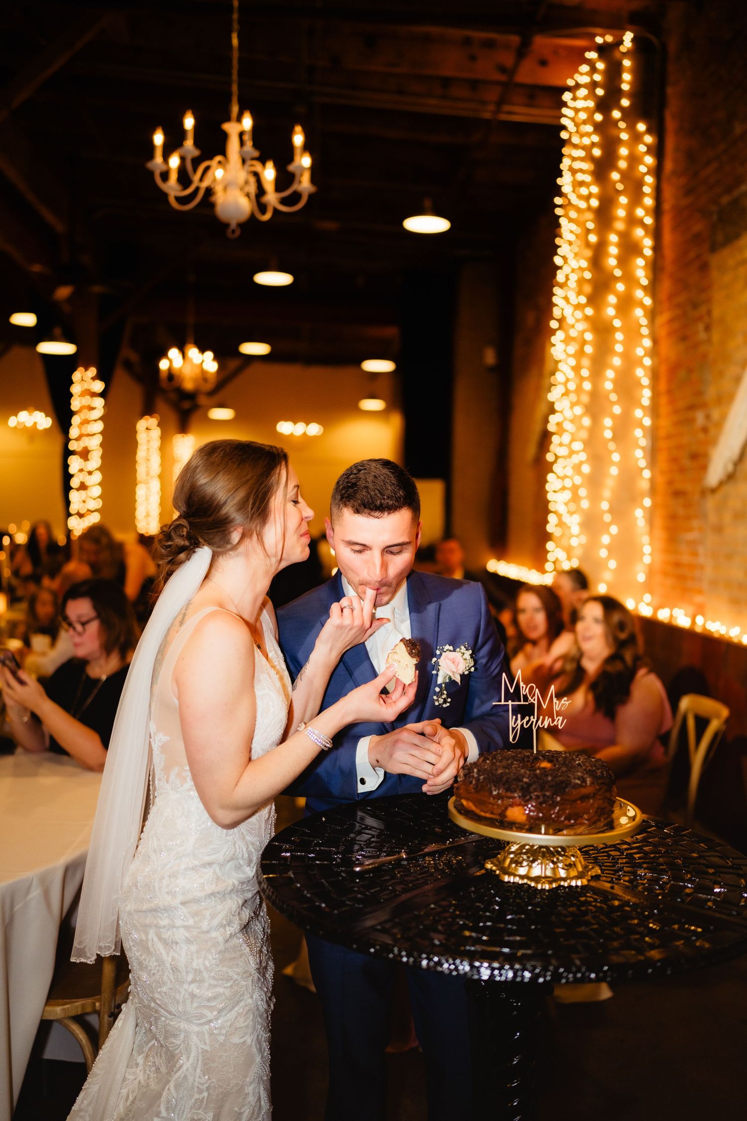 Bride and groom cutting their wedding cake at a romantic reception venue adorned with warm string lights.