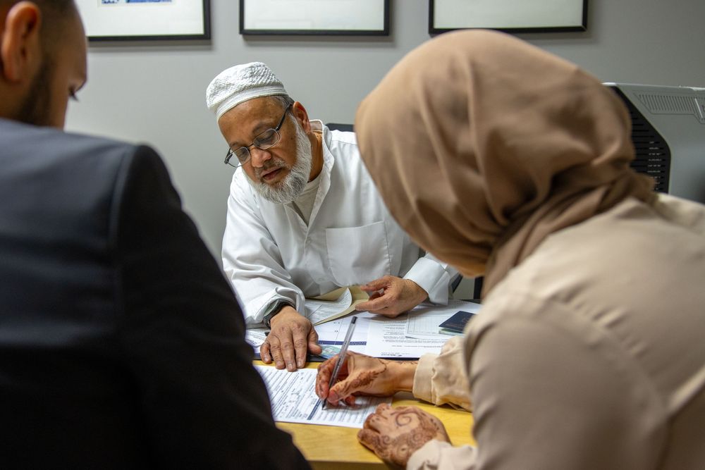 Muslim family signing legal documents with an imam at an office desk during a formal meeting.