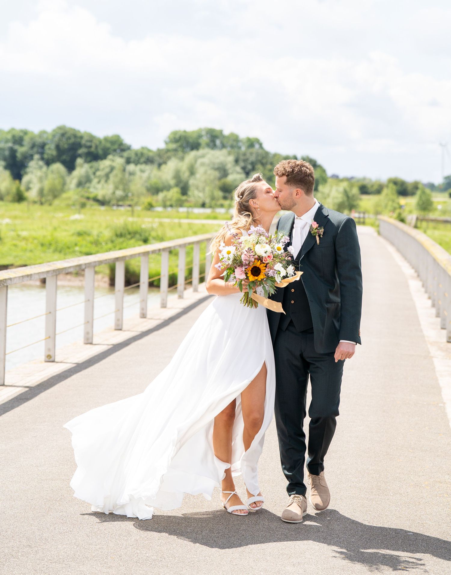 Bruid en bruidegom delen een romantisch moment onder bakstenen bogen; de bruid draagt ​​een zwierige witte jurk met een lange sluier.