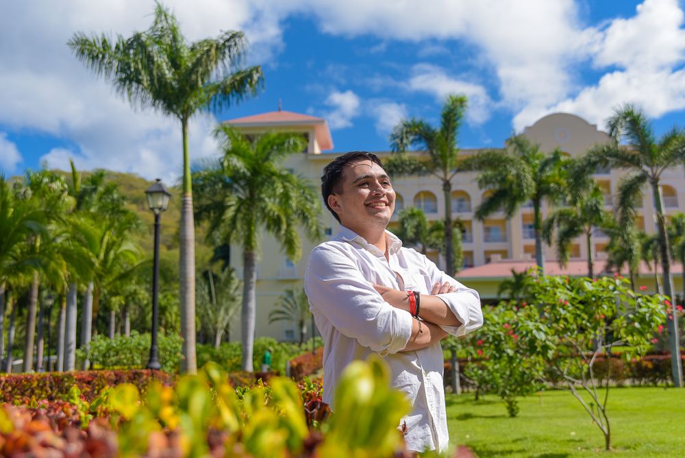 People gather for a group photo on a sunny day surrounded by lush palm trees and landscaped grounds.