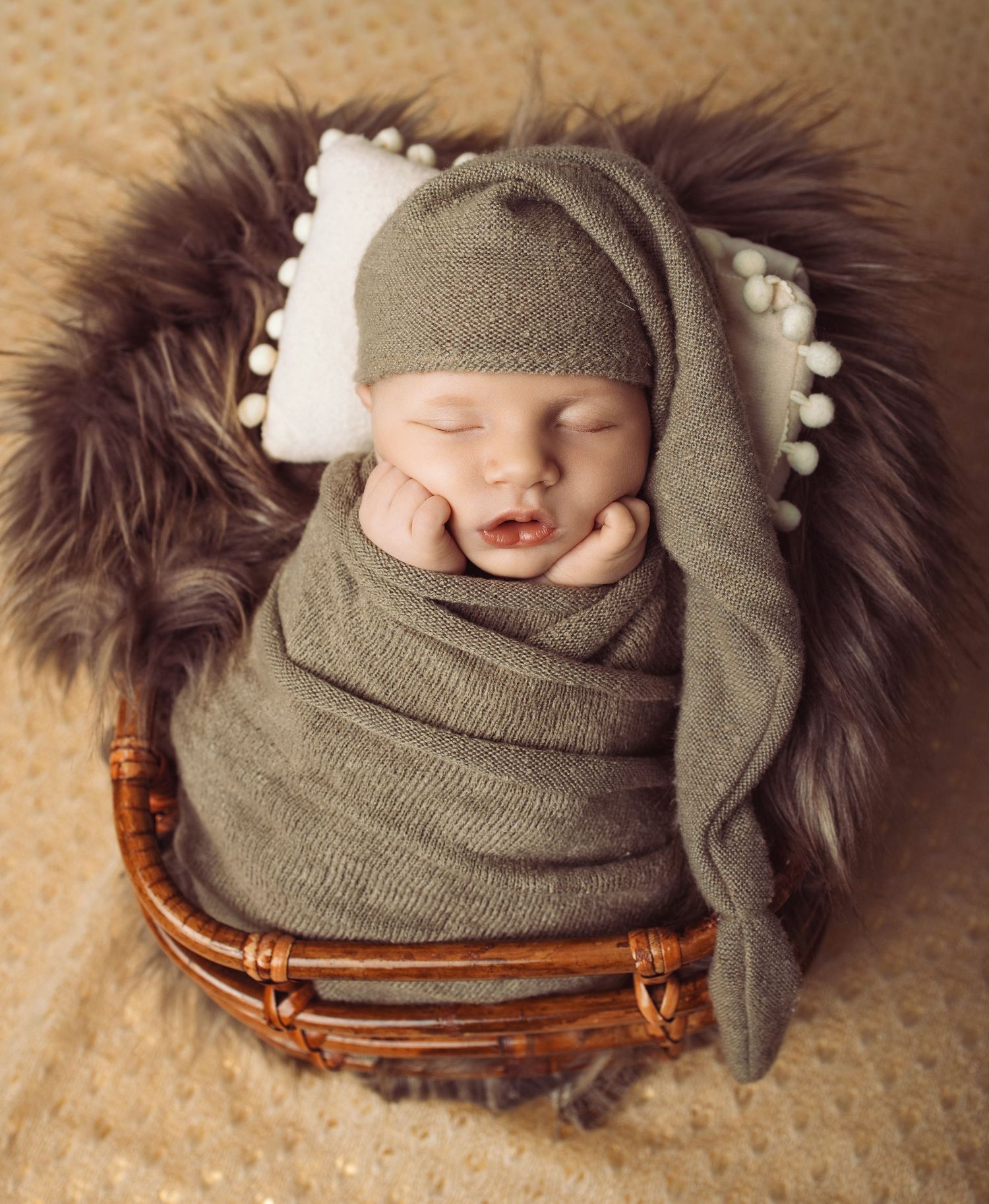 A sleeping baby in neutral tones lies on a beige blanket with plush toys arranged in a row.