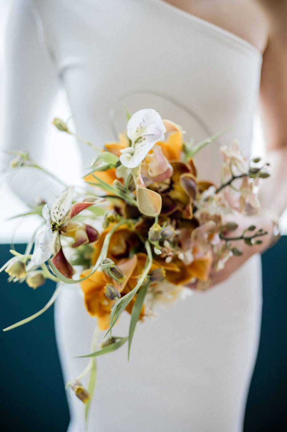 Close-up of organic orange and white floral bouquet against sleek white wedding dress.