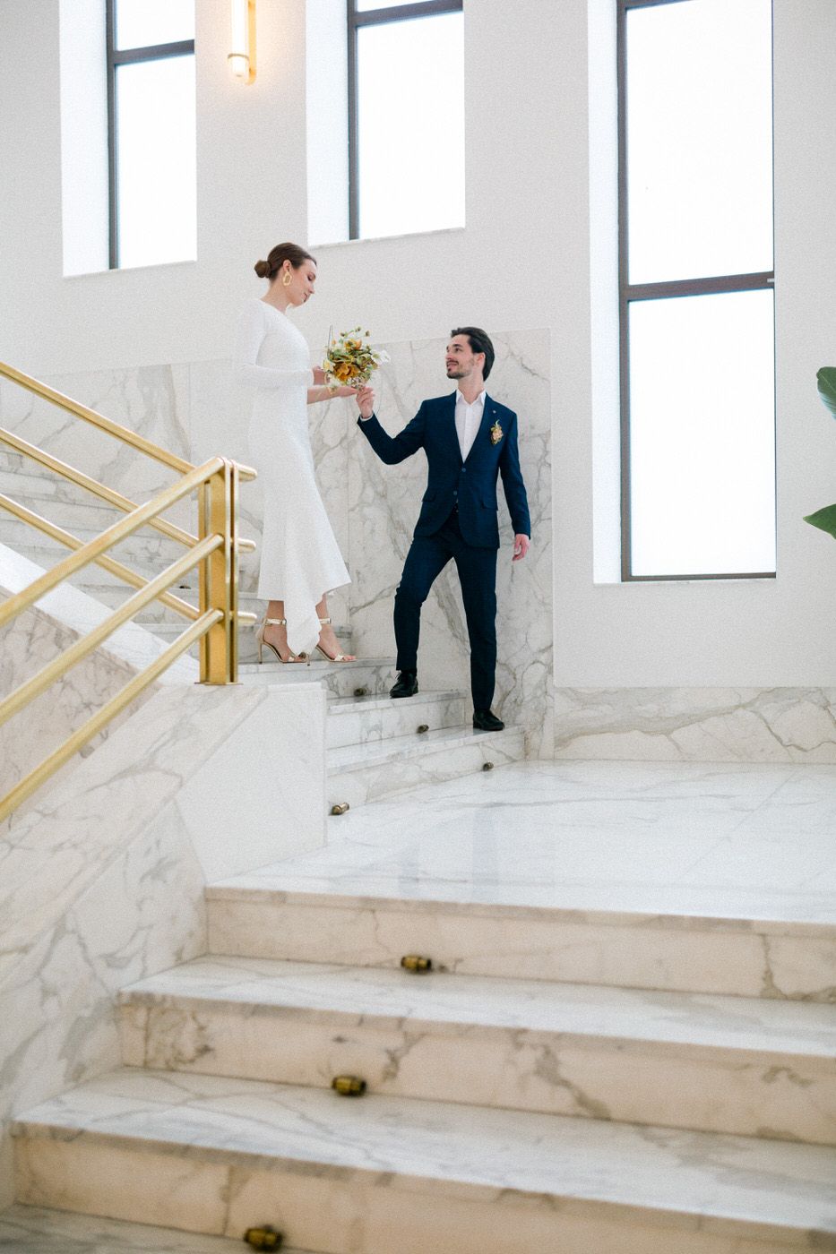 Elegant marble staircase scene with gold railings and tall windows in modern white interior.