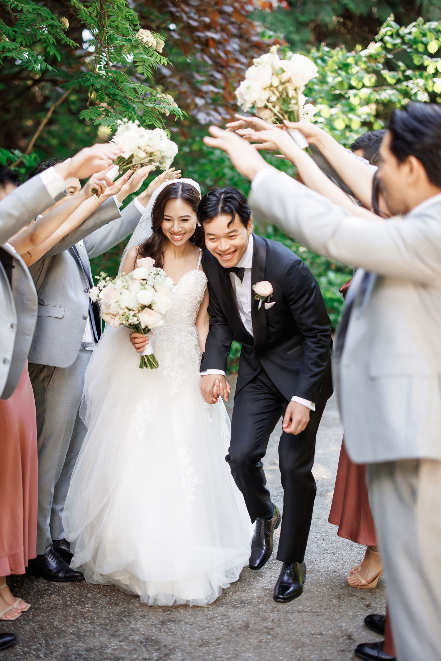 Wedding party members in formal attire lean and pose together playfully in an outdoor garden setting.Queen Elizabeth Park Wedding