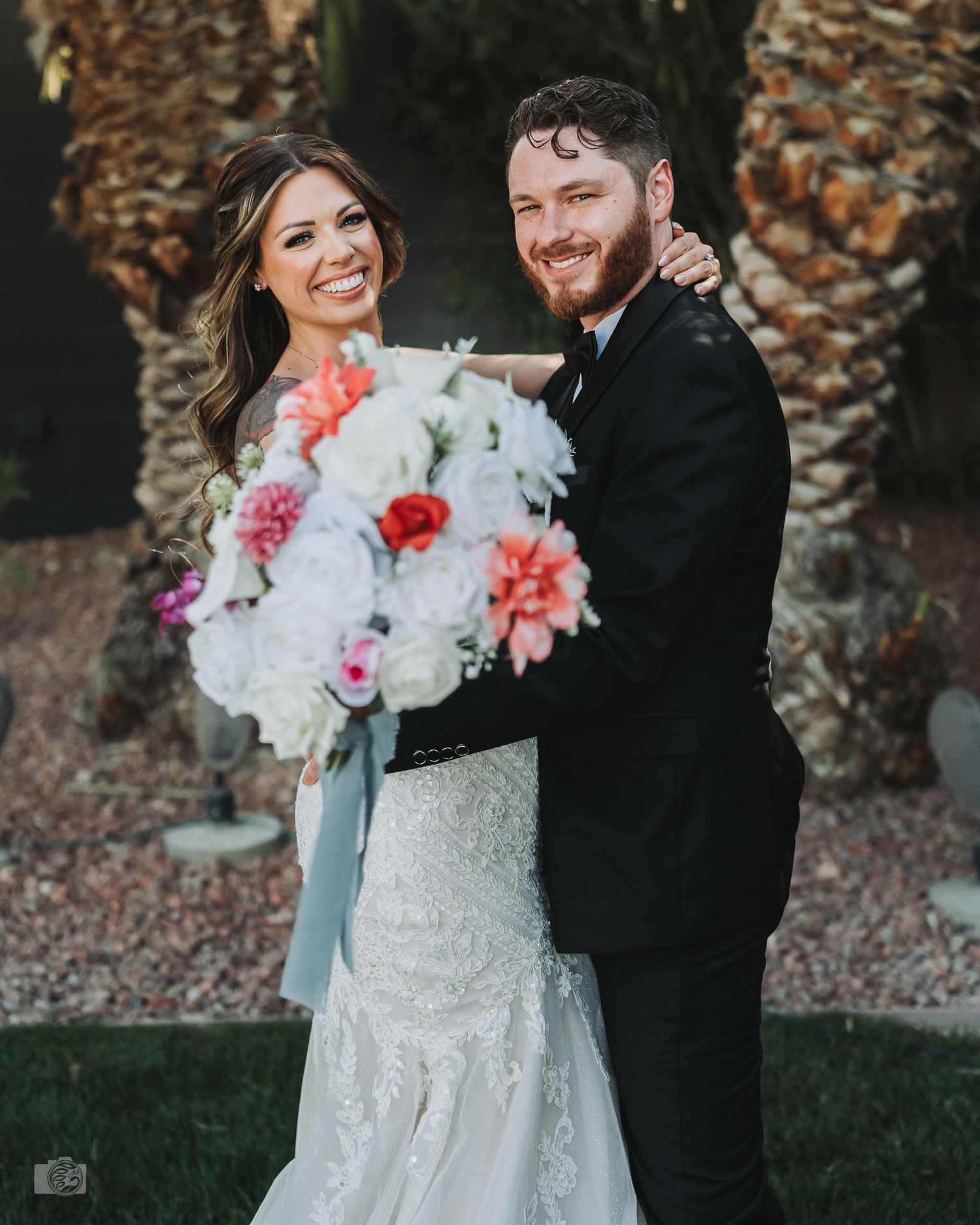 A stylish couple wearing sunglasses poses together in wedding attire.
