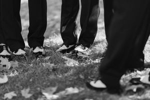 A row of shoes positioned on a grassy lawn in black and white, showing only people's feet and ankles.
